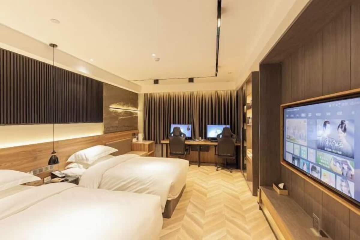Una habitación de hotel con dos camas, un escritorio con dos monitores, un televisor y un ventanal grande.