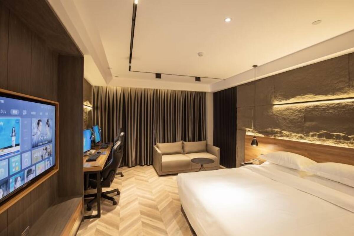 Una habitación de hotel moderna con una cama grande, un escritorio con una computadora, un sofá y un televisor montado en la pared.