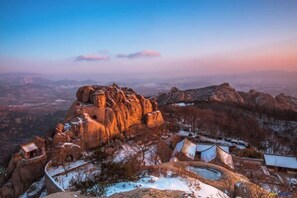 A mountainous landscape with a prominent rock formation and a small settlement with buildings. - Yunyi Art Hotel (Rizhao)