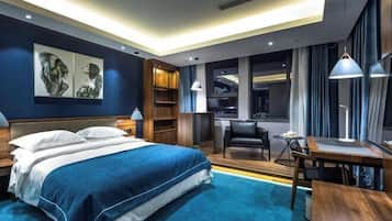 A modern hotel room with a large bed, a desk, a chair, a bookshelf, and a window with curtains.