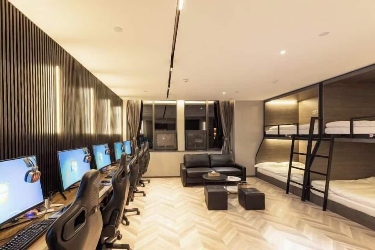 Una habitación de hotel moderna con un escritorio grande con múltiples monitores, un sofá, una cama litera y un piso con estampado de espiga.