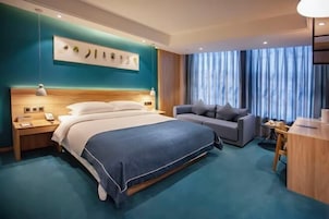A modern hotel room with a large bed, a sofa, a desk, and a large window with curtains.