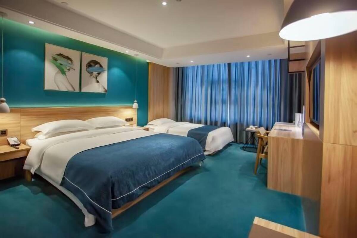 Habitación de hotel con dos camas, un escritorio, una silla y un ventanal con cortinas.