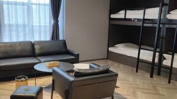 A modern hotel room with a sofa, a small round table, a chair, a bunk bed, and a window with curtains.