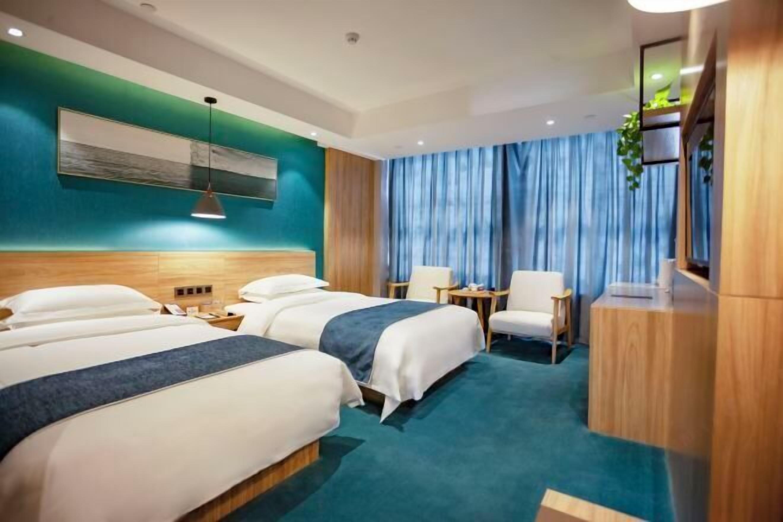 A hotel room with two beds, a desk, a chair, a TV, and a large window with curtains.