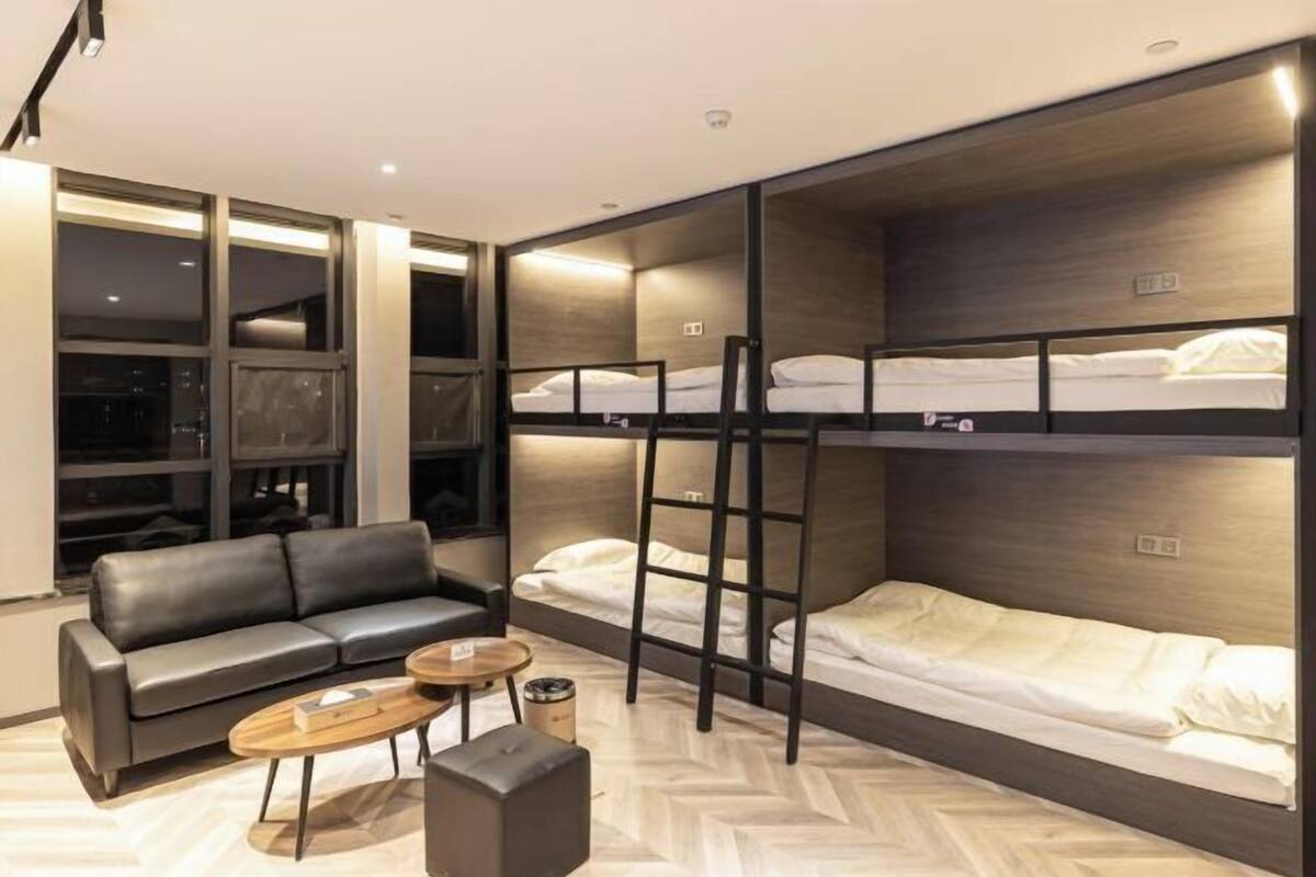 Una habitación de hotel moderna con sofá, una mesa de centro, literas y vistas amplias a través de grandes ventanales.