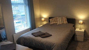 A neatly made bed with a grey blanket and two pillows, two bedside lamps, and a window with a view of buildings. - Berlin Town house Belfast (Belfast)