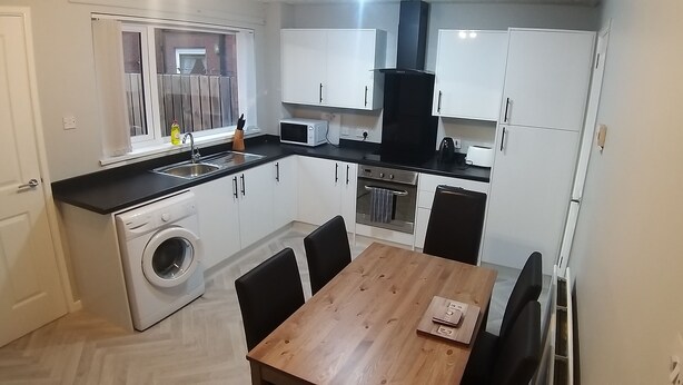 A compact kitchen with a washing machine, a microwave, and a stove. There is a wooden table and chairs. - Berlin Town house Belfast (Belfast)