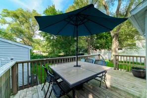 Relax on the outdoor deck with a table and chairs under a spacious umbrella, taking in the view of the surrounding neighborhood.