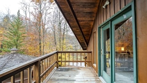 A wooden deck with a railing, a large window, and a view of autumn trees. - Base Camp (Davis)