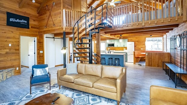 A spacious living area with a leather sofa, a wooden staircase, and a kitchen in the background. - Base Camp (Davis)