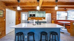A kitchen with wooden beams, a central island with stools, a refrigerator, and a window with a view. - Base Camp (Davis)