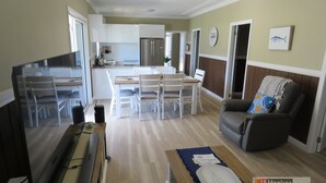 A modern apartment with a dining area, kitchen, and living room. - BROWNY'S R & R - Beach Cottage (South West Rocks)