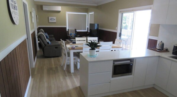 A modern kitchen with white cabinetry, a built-in oven, and a dining area with a table and chairs.
