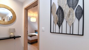 Un dormitorio moderno con cama, lámpara de noche, espejo en la pared y una obra de arte decorativa con hojas.