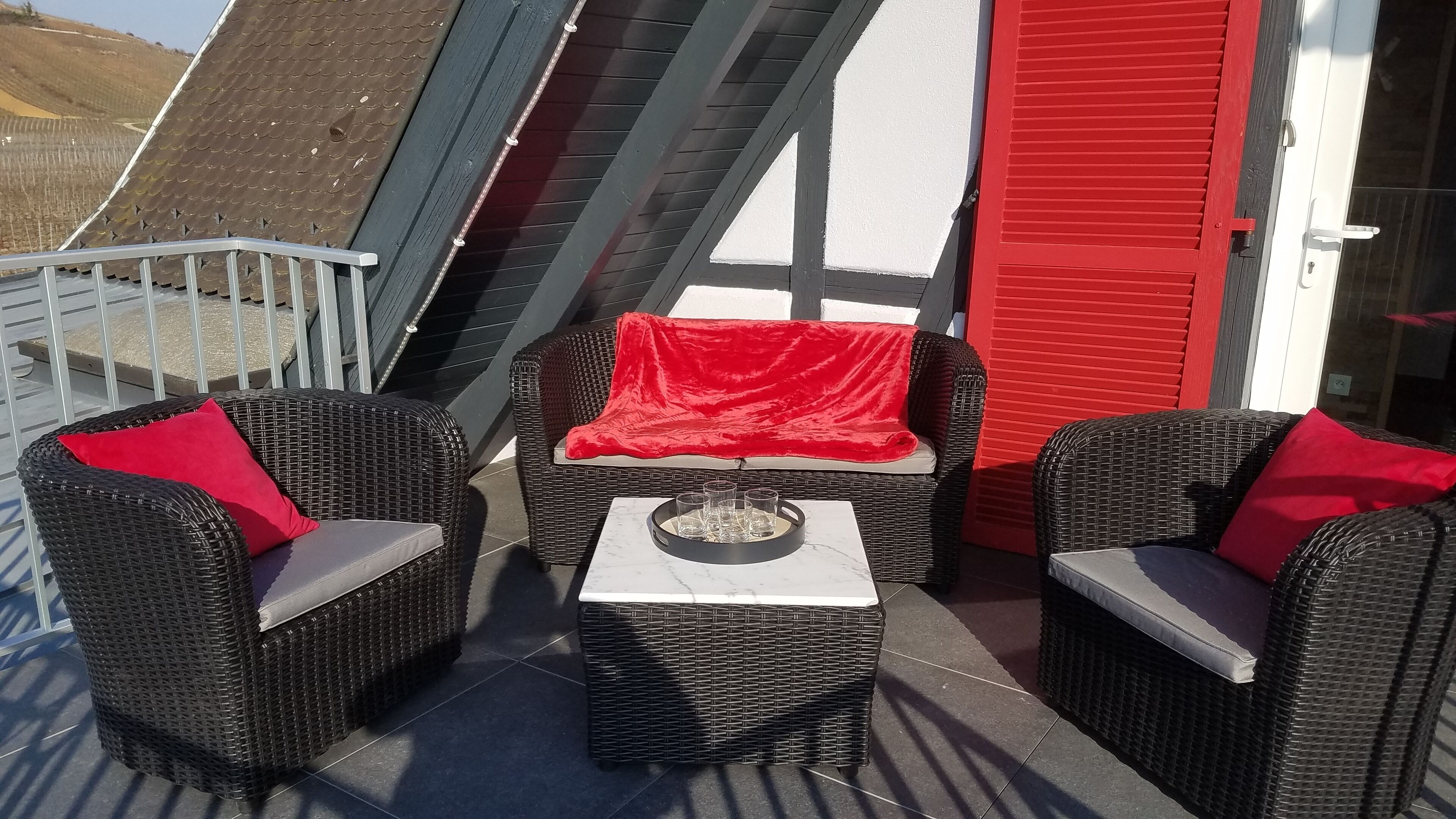 A balcony with wicker furniture, a small table, and a red chair.