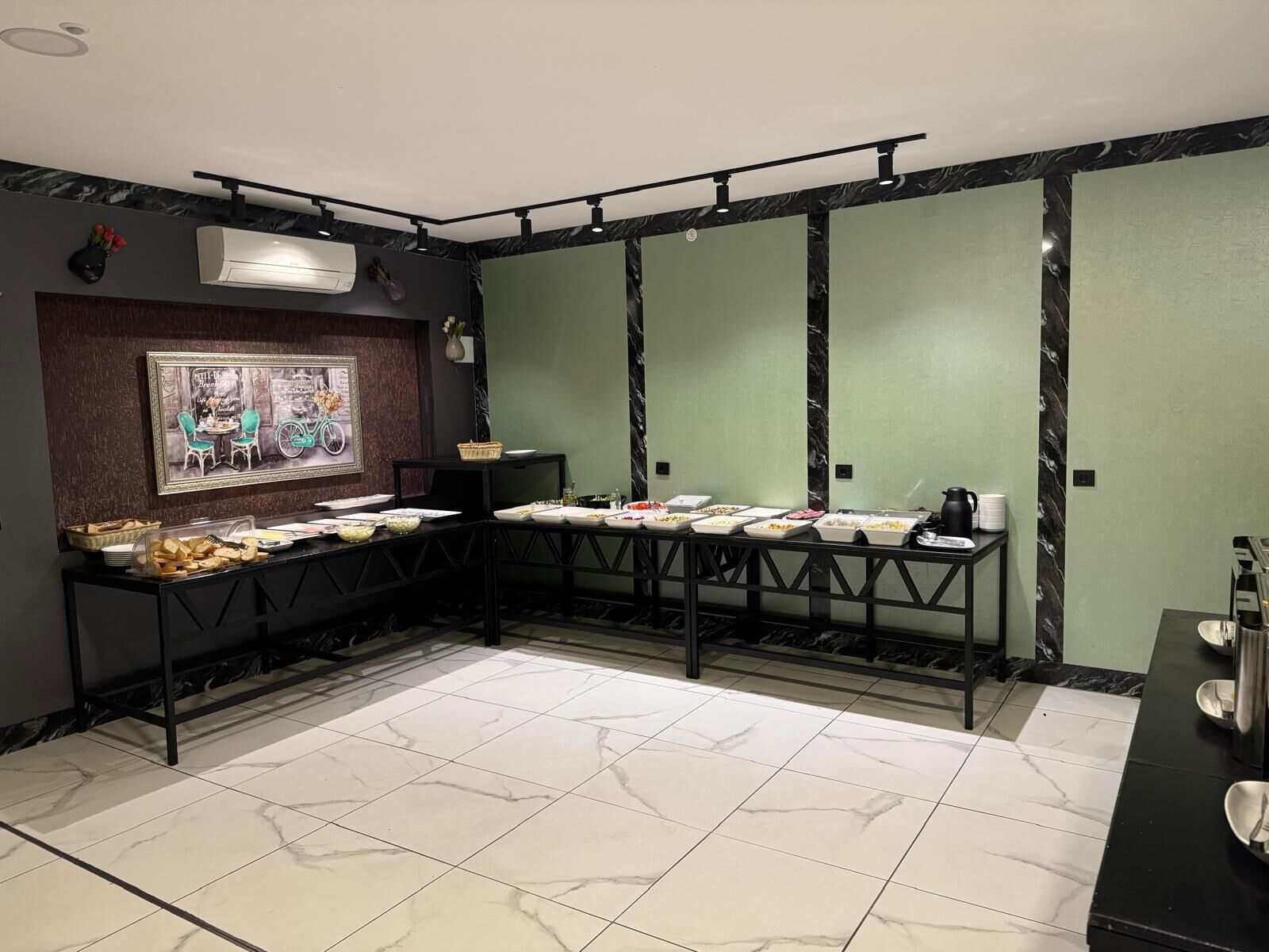 Une pièce avec une longue table dressée pour un repas, un climatiseur fixé au mur et un tableau encadré accroché au mur.