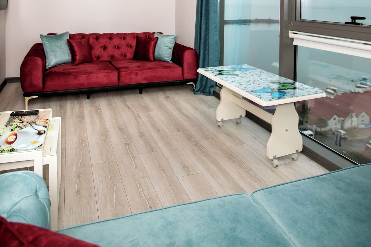 Un salón moderno con un sofá rojo, una mesita y vistas al mar a través de amplios ventanales.