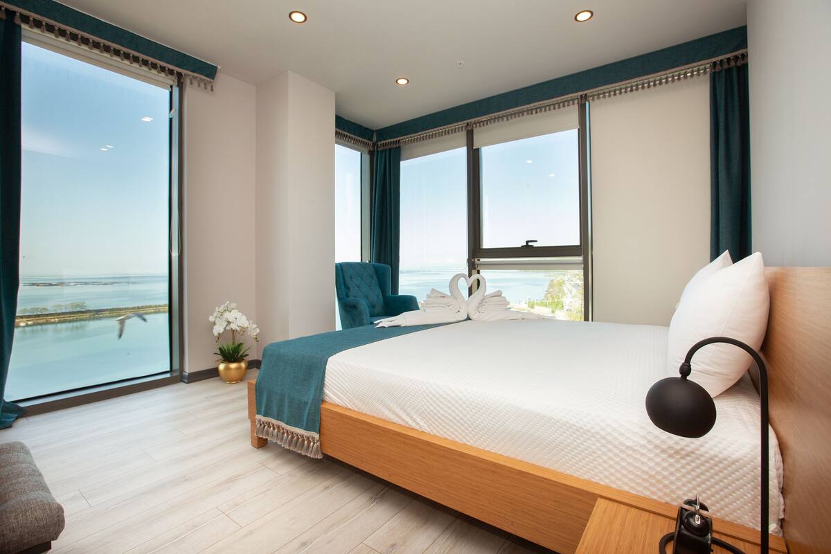 Un dormitorio con una cama grande, una silla, una mesita de noche, una lámpara y vistas al mar.