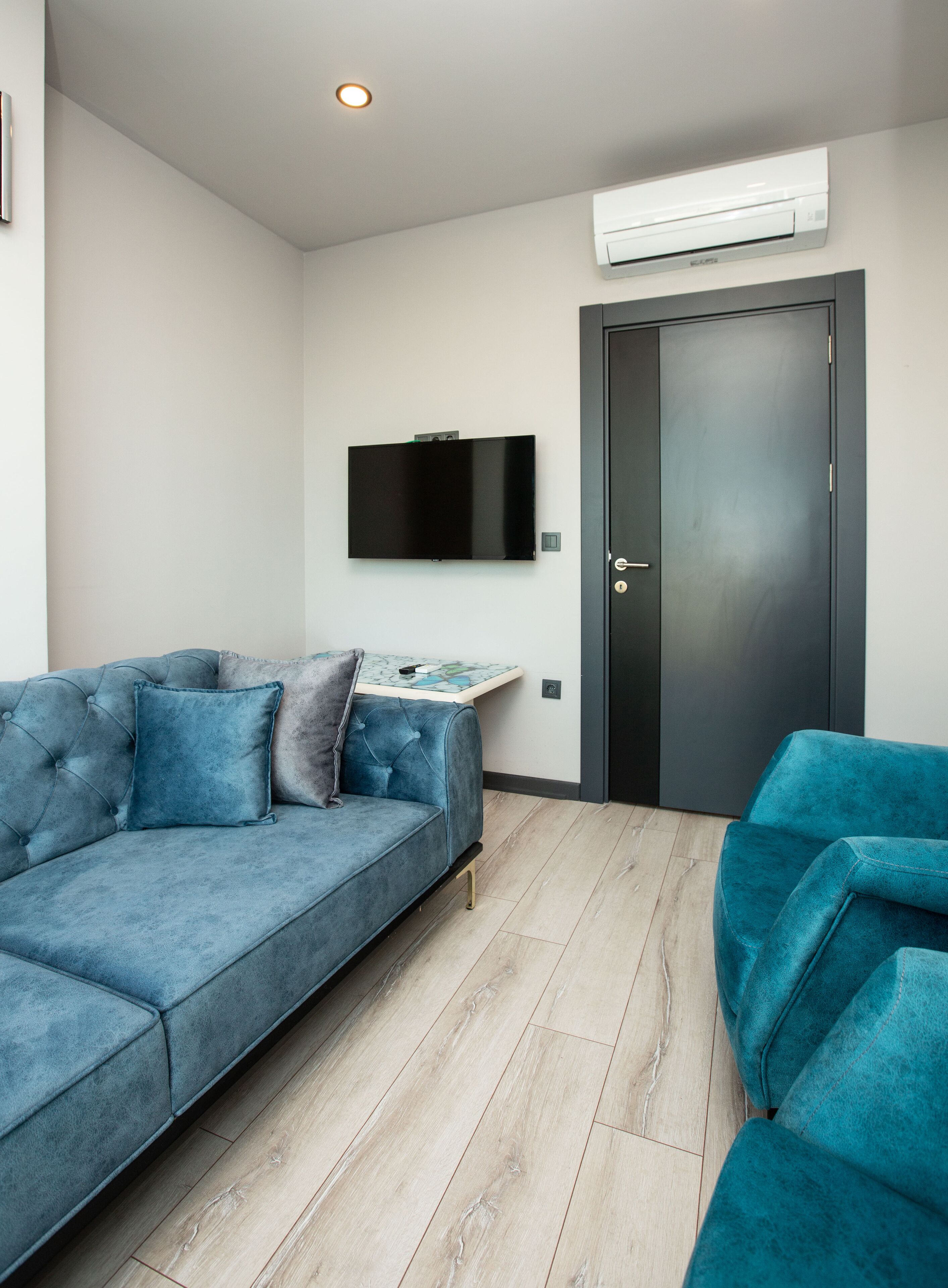 Una sala de estar moderna con un sofá azul, un sillón azul más pequeño, un televisor de pantalla plana montado en la pared y una puerta con manija.