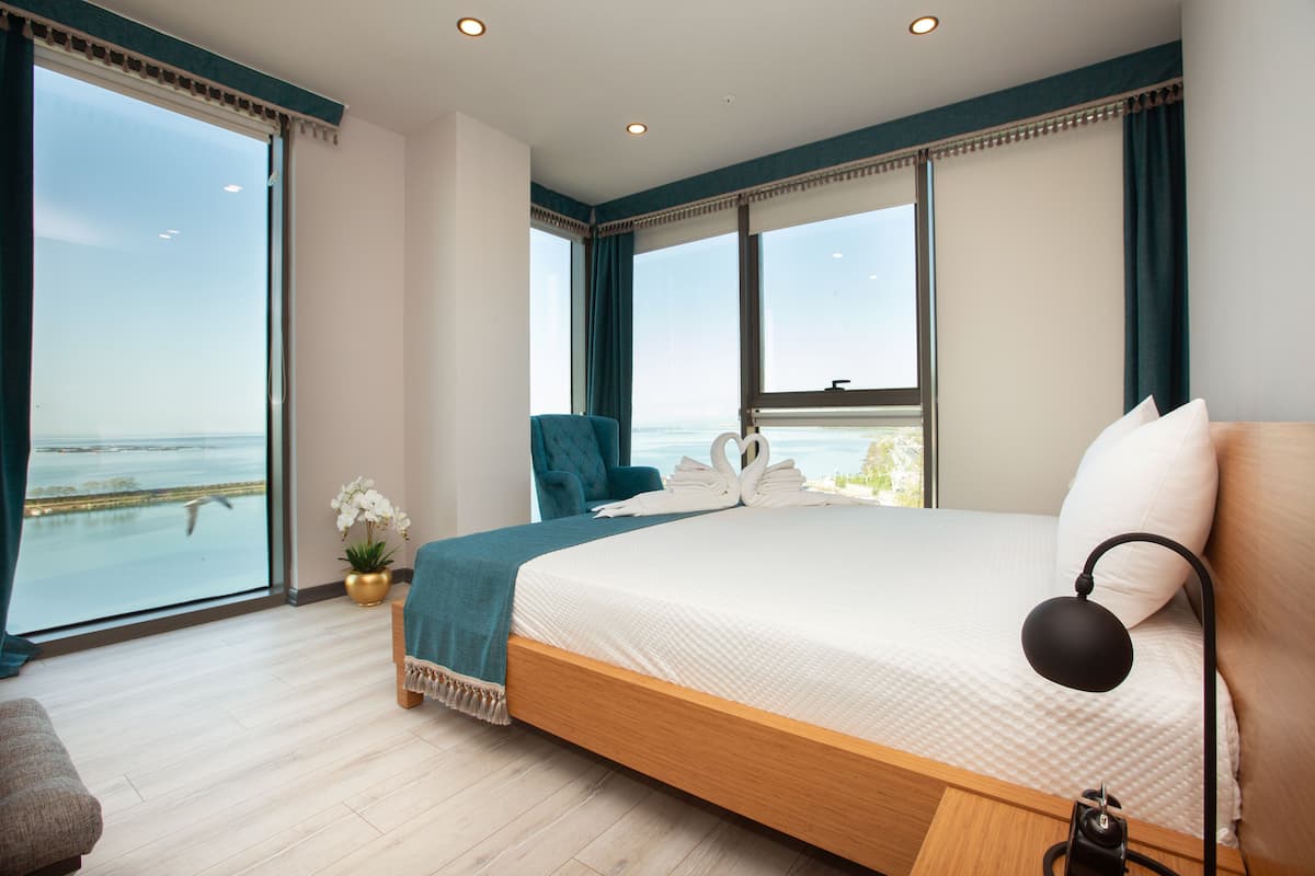 Un dormitorio con una cama grande, una silla, un escritorio y vista al mar.