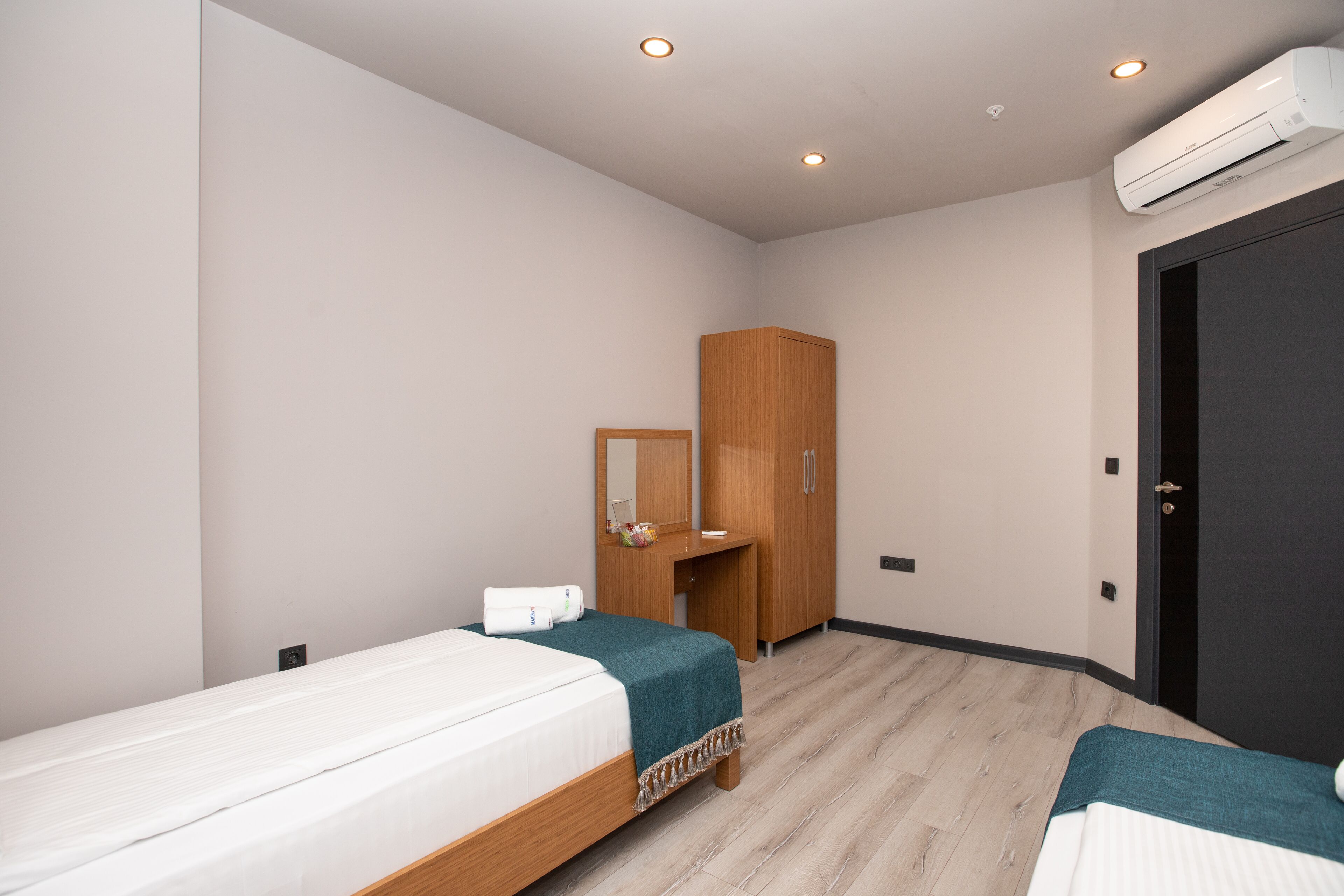Habitación de hotel con dos camas individuales, un armario de madera, un espejo y un equipo de aire acondicionado.