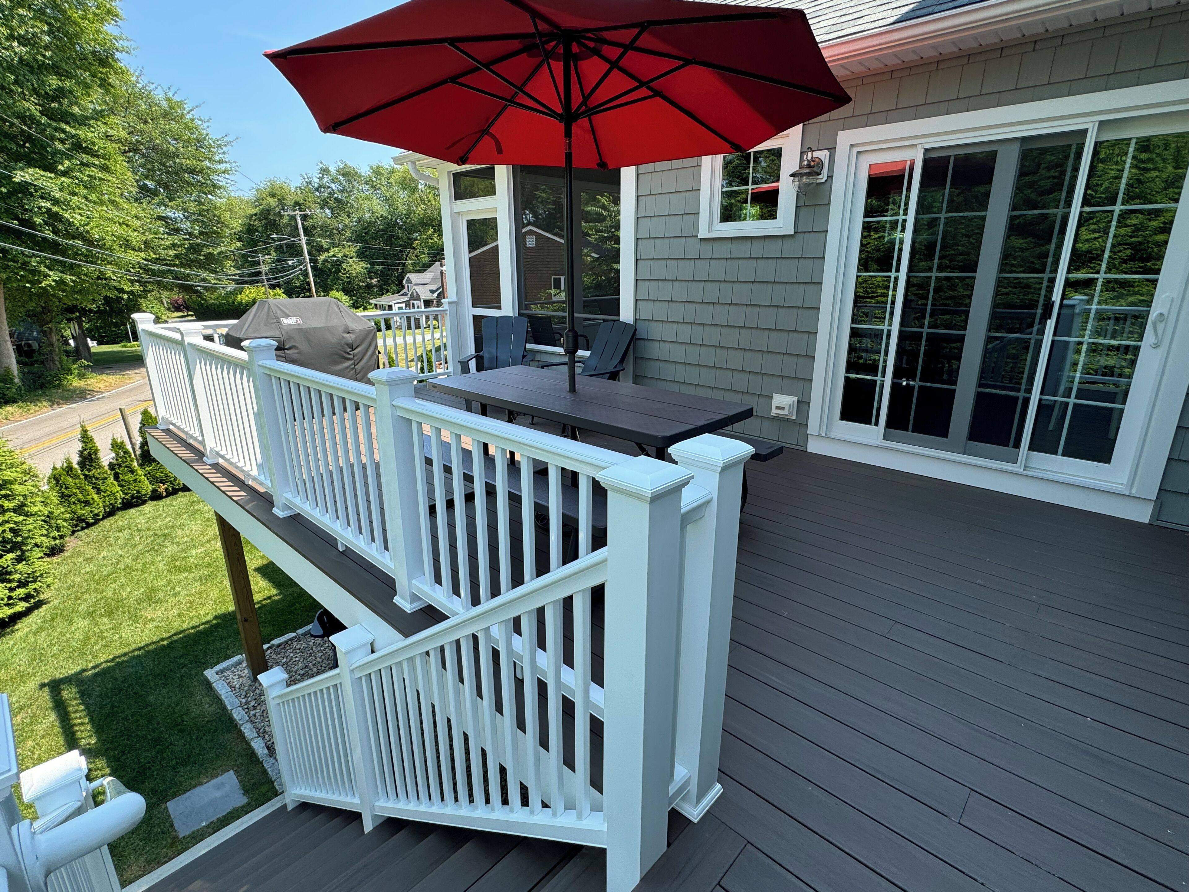 A deck with a table and chairs, a red umbrella, and a white railing.