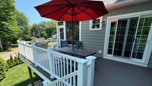 A deck with a table and chairs, a red umbrella, and a white railing.
