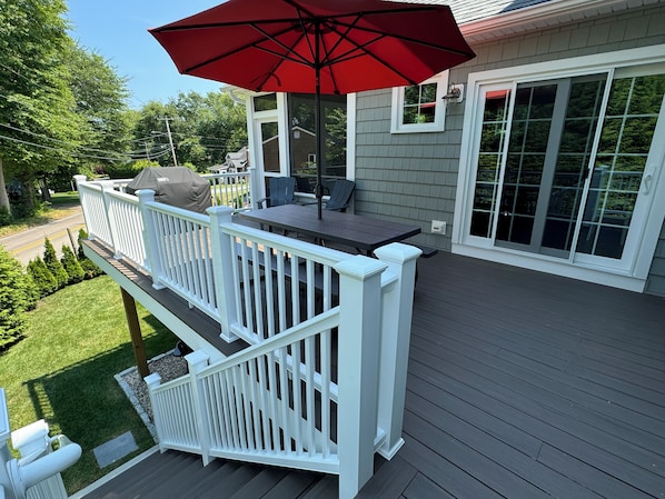 A deck with a table and chairs, a red umbrella, and a white railing. - The Cottage in Bonnet Shores Private Beach Community (Narragansett)