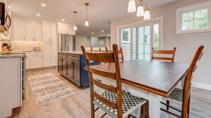 A modern kitchen with white cabinets, a central island, and a dining area with wooden chairs and a table.