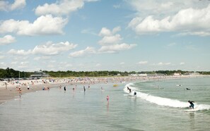 A crowded beach with people swimming and surfing, and a clear sky. - The Cottage in Bonnet Shores Private Beach Community (Narragansett)