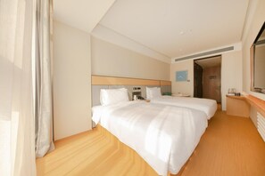 Ein Hotelzimmer mit zwei Betten, einem Nachttisch mit Lampe, einem kleinen Schreibtisch und einem großen Spiegel.
