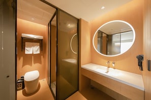 A modern bathroom with a glass partition, a round mirror, a white sink, and a toilet.
