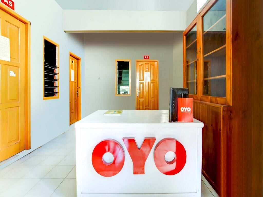 A reception desk with the OYO logo, wooden doors, and a tiled floor.