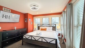 A hotel room with a bed, a dresser, a vanity, and a large window with blinds. - Rock N Rooftop W/Skyline Views+80 in tv, Pinball, Shuffleboard and more! (Cleveland)