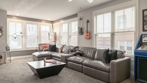 A modern living room with a sectional sofa, a coffee table, and a gaming console. - Rock N Rooftop W/Skyline Views+80 in tv, Pinball, Shuffleboard and more! (Cleveland)