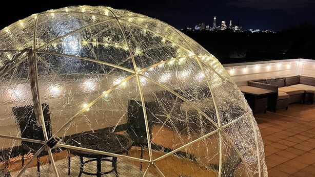 A transparent dome structure with a table and chairs inside, overlooking a cityscape at night. - Rock N Rooftop W/Skyline Views+80 in tv, Pinball, Shuffleboard and more! (Cleveland)
