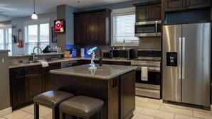 A modern kitchen with dark wood cabinets, stainless steel appliances, a granite countertop, and two bar stools. - Rock N Rooftop W/Skyline Views+80 in tv, Pinball, Shuffleboard and more! (Cleveland)