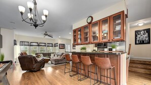 Una cocina moderna con armarios de madera, una barra con taburetes y una zona de comedor con mesa de billar.