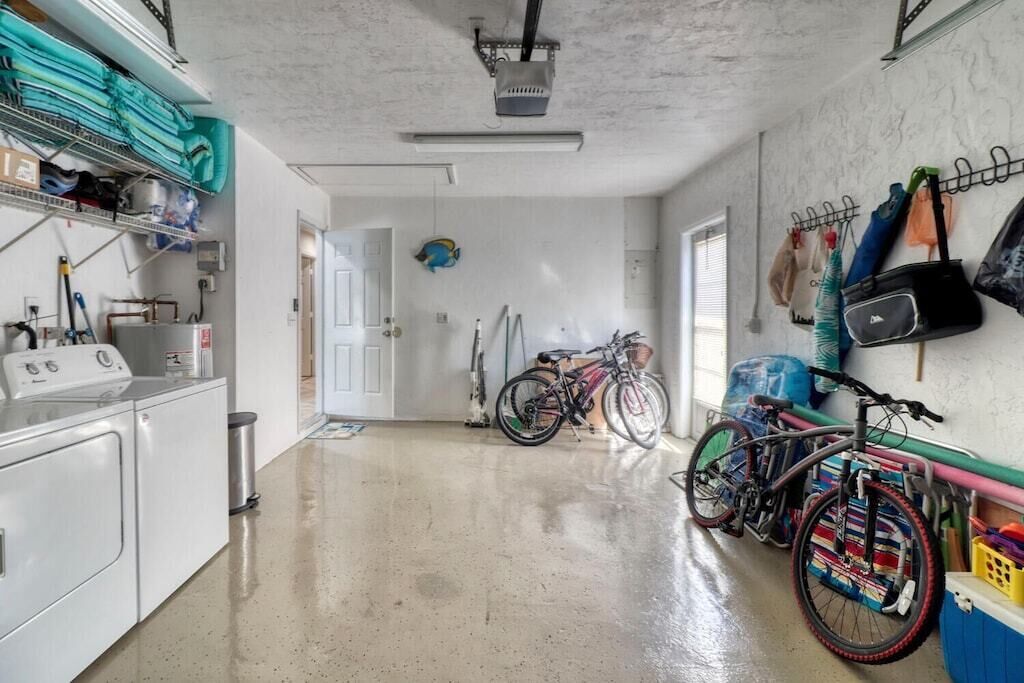 A laundry room with a washing machine, dryer, and shelves with folded clothes. There are bicycles parked against the wall and a door leading to another room.