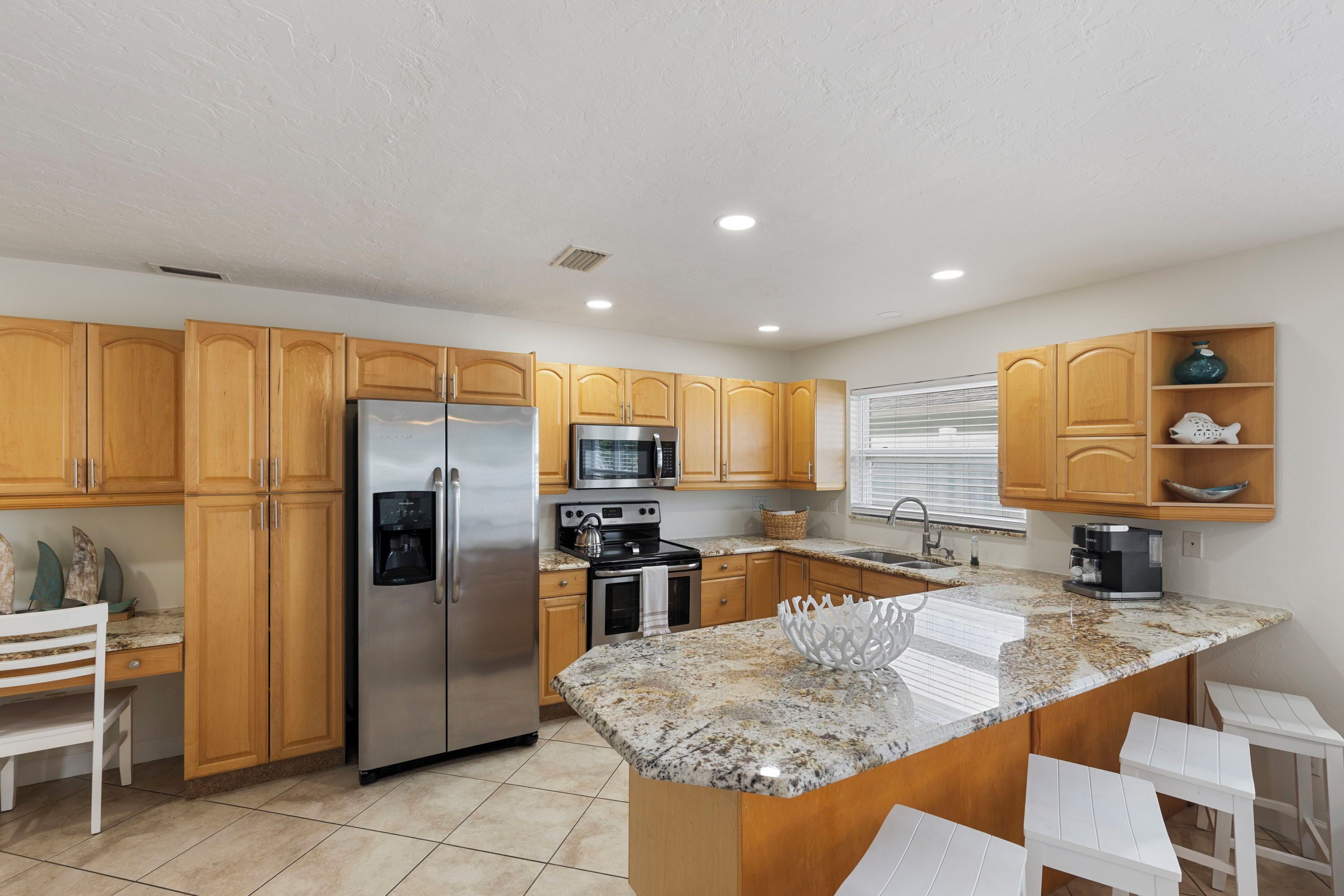 A kitchen with wooden cabinets, stainless steel appliances, a granite countertop, and a white bar stool area.