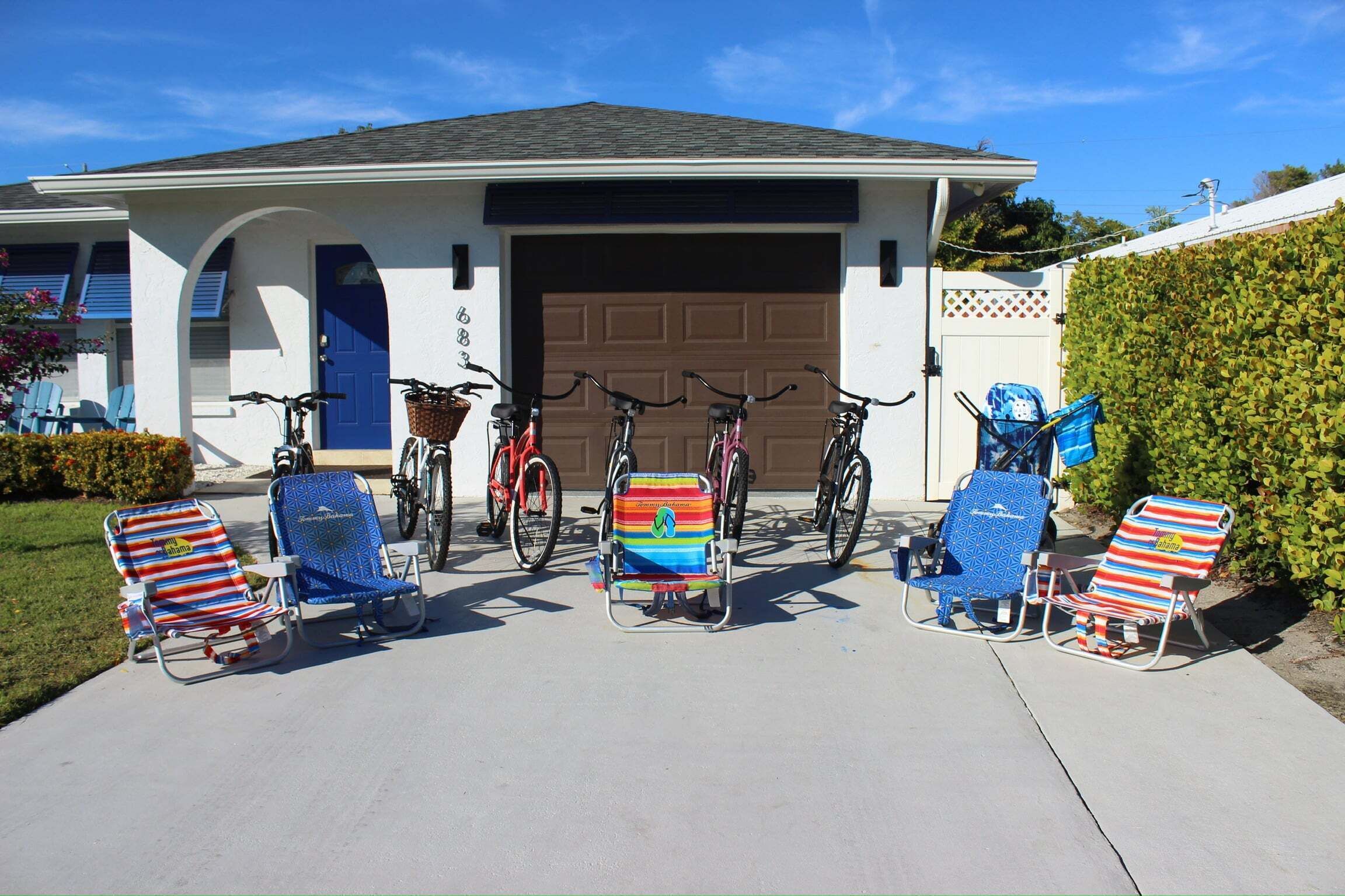 A house with a garage, a driveway, and several beach chairs and bicycles.