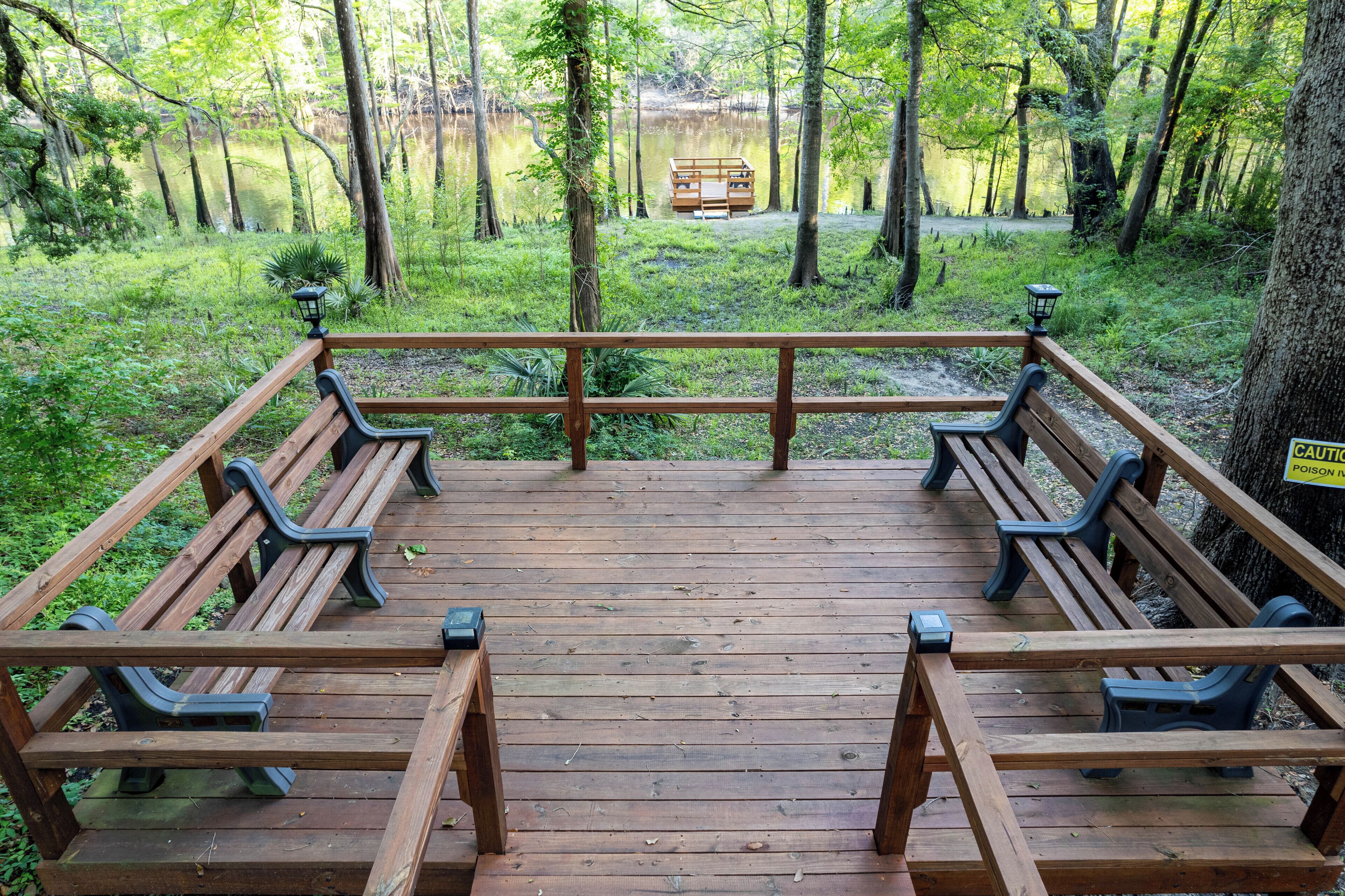 A wooden deck with benches overlooking a forested area and a lake.