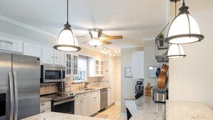 Cocina moderna con encimeras de granito, electrodomésticos de acero inoxidable e iluminación colgante.