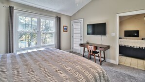 Un dormitorio con una cama grande, un escritorio, una silla, un televisor y una puerta que da a otra habitación.