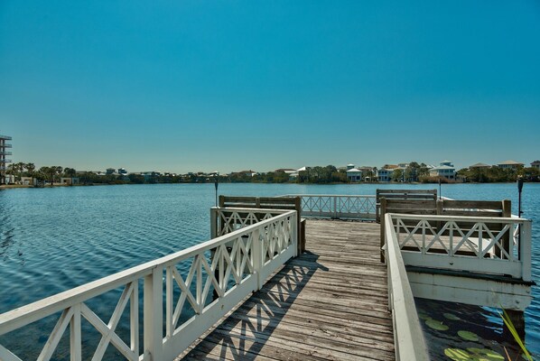 A wooden pier leading to a dock with a white railing, extending over calm water.