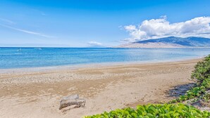 A beach with clear blue water, a sandy shore, and mountains in the background. - Walk To Beach! Beautiful Ocean Views from Condo W/ Lanai, Pool & Hot Tub, BBQ (Kihei)