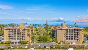 A hotel with multiple floors, outdoor parking, and a view of the ocean. - Walk To Beach! Beautiful Ocean Views from Condo W/ Lanai, Pool & Hot Tub, BBQ (Kihei)