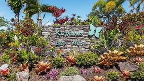 A sign for Kapulua Bay Villas surrounded by tropical plants and a clear blue sky. - Steps from Merriman's, Your Kapalua Villa stay (Lahaina)