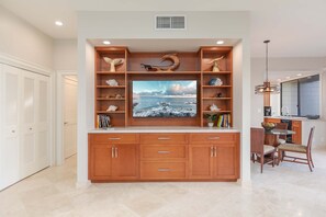 A modern kitchen with wooden cabinetry, a central island, and a large flat-screen TV above the cabinetry.